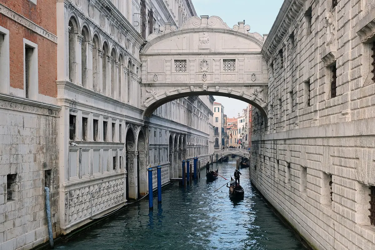 El arco de piedra caliza blanca del Puente de los Suspiros, tendido entre dos edificios de piedra sobre un estrecho canal de Venecia, con una góndola debajo